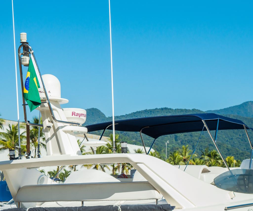 A imagem mostra um closeup no topo de uma lancha estacionada na marina guararu com montanhas verdes ao fundo em um dia ensolarado.